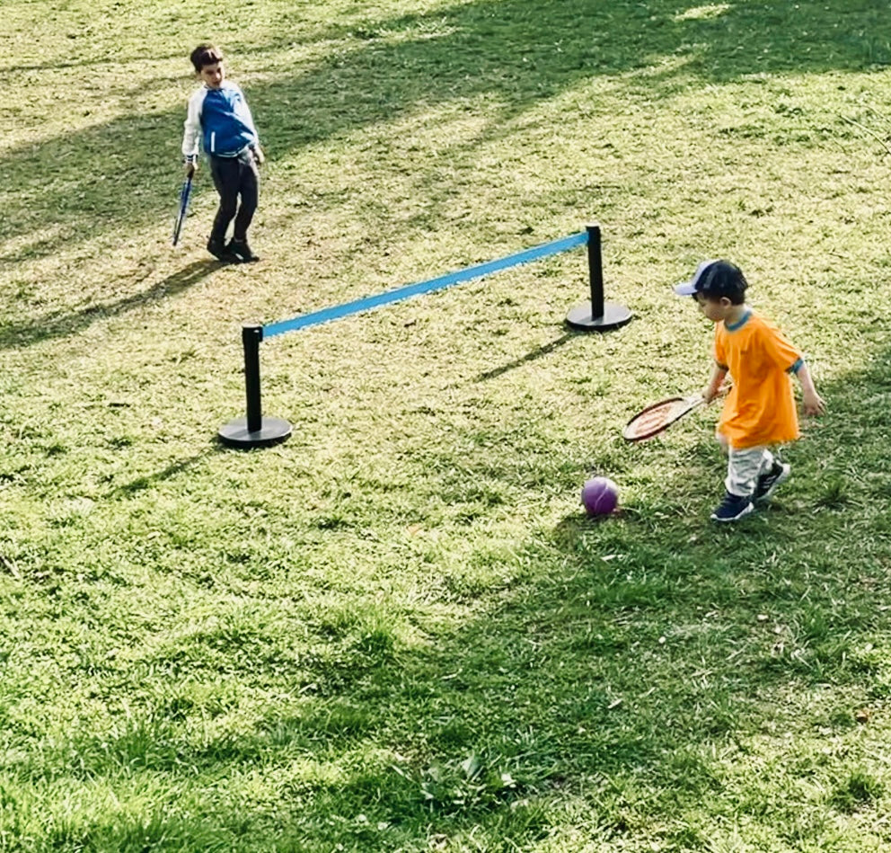 Two young children playing tennis over a low ground-level net in a garden