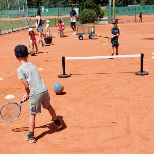 Kindertennis-Training auf dem Sandplatz: Kind schlägt den rollenden Ball über das WHACK! Rollo Netz